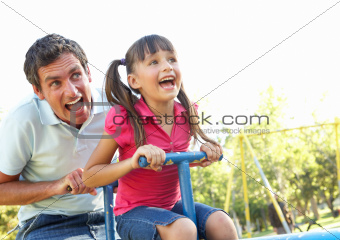 Father And Daughter Riding On See Saw In Playground
