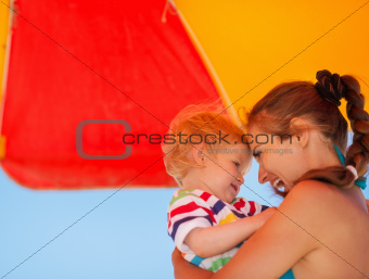 Portrait of mother and baby on beach under umbrella