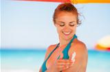 Happy woman applying sun screen creme on arm