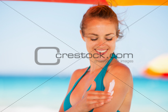 Happy woman applying sun screen creme on arm
