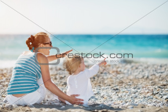 Mother and baby on beach pointing on copy space
