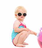 Baby in swimsuit and sunglasses playing with ball