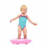 Baby girl in swimsuit standing in inflatable ring