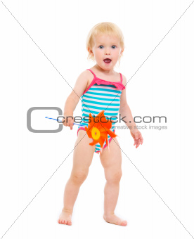 Surprised baby girl in swimsuit with pinwheel