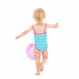 Baby girl in swimsuit playing with ball. Rear view