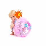 Baby in swimsuit with pinwheel hiding behind beach ball