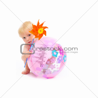Baby in swimsuit with pinwheel hiding behind beach ball