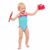 Cheerful baby girl in swimsuit with bucket and shovel