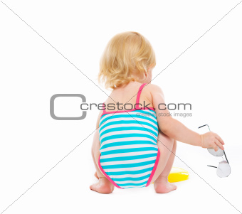 Sitting baby in swimsuit with sun glasses. Rear view
