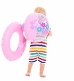Baby in swimsuit with inflatable ring hiding behind beach ball