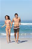 Young Couple Running On Beach Wearing Swimwear