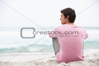 Young Man On Holiday Sitting On Winter Beach