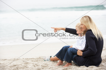 Mother And Daughter On Holiday Sitting On Winter Beach