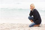 Young Woman On Holiday Kneeling On Winter Beach