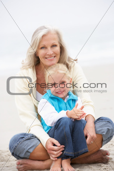 Grandmother And Granddaughter On Holiday Sitting On Winter Beach