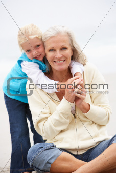 Grandmother And Granddaughter On Holiday Sitting On Winter Beach