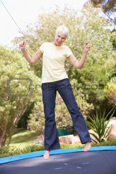 Senior Woman Jumping On Trampoline In Garden