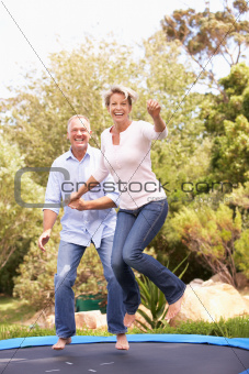 Couple Jumping On Trampoline In Garden