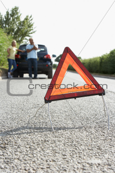 Couple Broken Down On Country Road With Hazard Warning Sign In Foreground