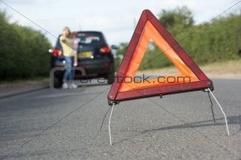 Mother And Daughter Broken Down On Country Road With Hazard Warning Sign In Foreground