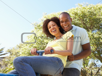 Portrait Of Young Couple Riding On SeeSaw In Park