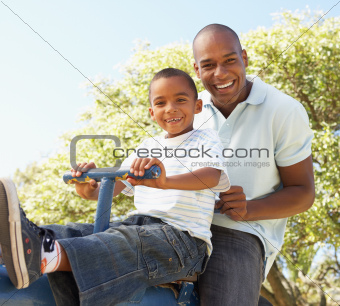 Father and Son Riding On SeeSaw In Park