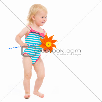 Happy baby in swimsuit with pinwheel looking on copy space