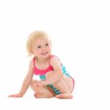 Curious baby in swimsuit sitting on floor and looking on copy space
