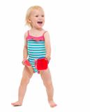 Cheerful baby in swimsuit playing with bucket and shovel