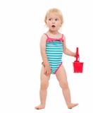 Surprised baby in swimsuit playing with bucket and shovel