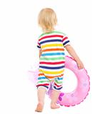 Baby in swimsuit playing with inflatable ring and beach ball. Rear view