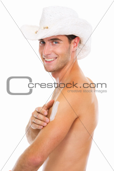 Smiling guy in hat applying sun block creme on arm