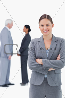 Smiling businesswoman with arms folded and colleagues behind her