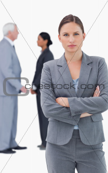Serious businesswoman with folded arms and colleagues behind her