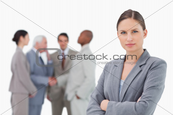 Serious saleswoman with arms folded and colleagues behind her