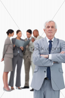 Mature businessman with arms folded and colleagues behind him