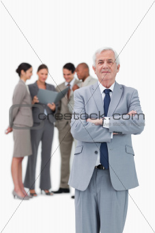 Mature businessman with arms folded and team behind him