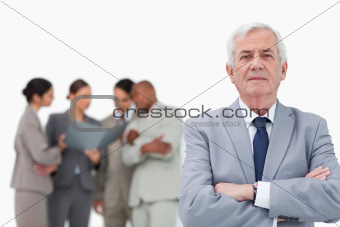 Mature salesman with arms folded and team behind him