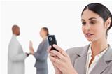Businesswoman looking at cellphone with colleagues behind her