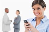 Smiling saleswoman holding mobile phone with colleagues behind her