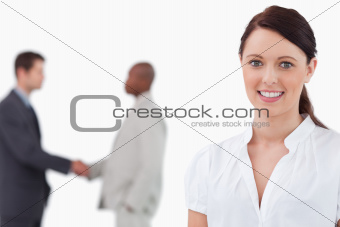 Smiling saleswoman with hands shaking trading partners behind her
