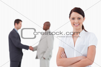 Businesswoman with arms folded and hand shaking trading partners behind her