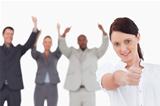 Businesswoman with cheering colleagues behind her giving thumb up