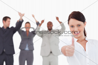 Saleswoman with cheering colleagues giving thumb up