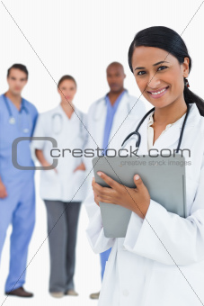 Smiling female doctor with clipboard and staff behind her