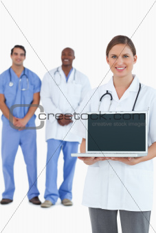 Smiling doctor showing laptop with colleagues behind her