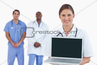 Smiling doctor showing notebook with colleagues behind her