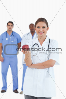 Smiling doctor with apple and colleagues behind her