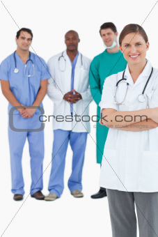 Smiling doctor with folded arms and colleagues behind her