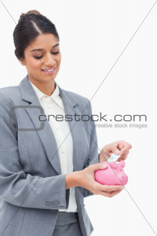 Smiling bank assistant putting bank note into piggy bank